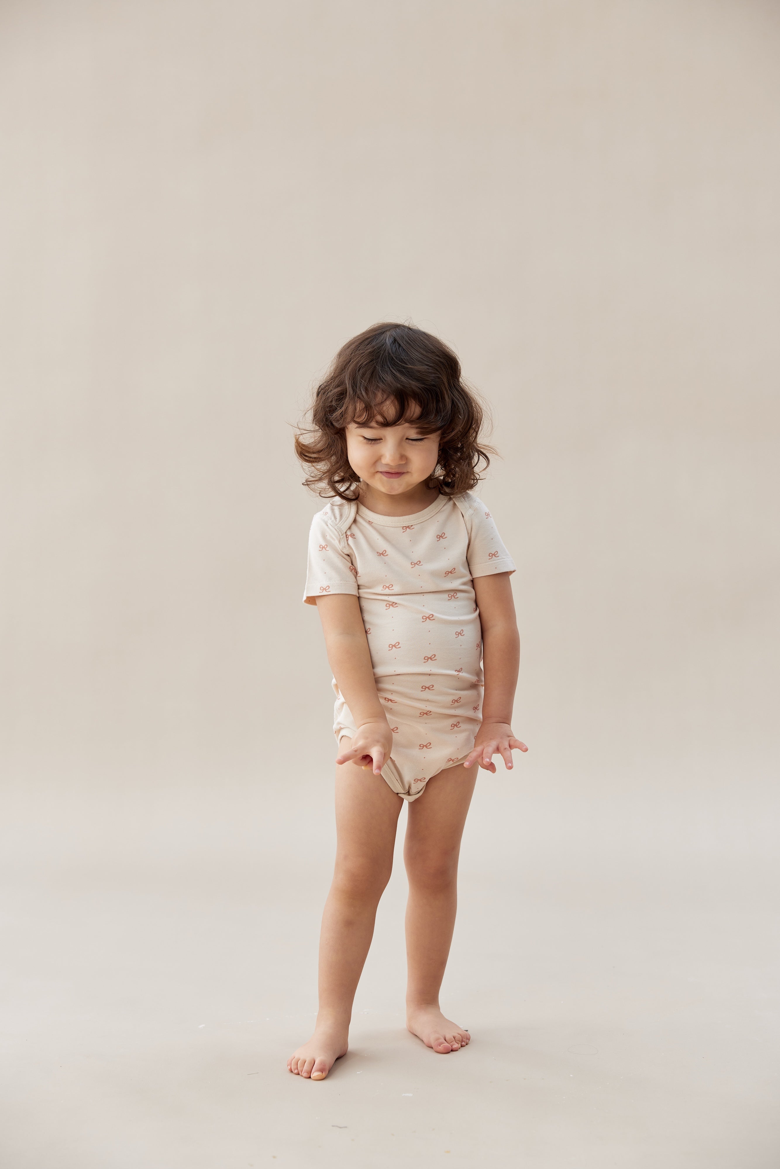 Child wearing a beige organic cotton onesie with a subtle pattern on a plain background