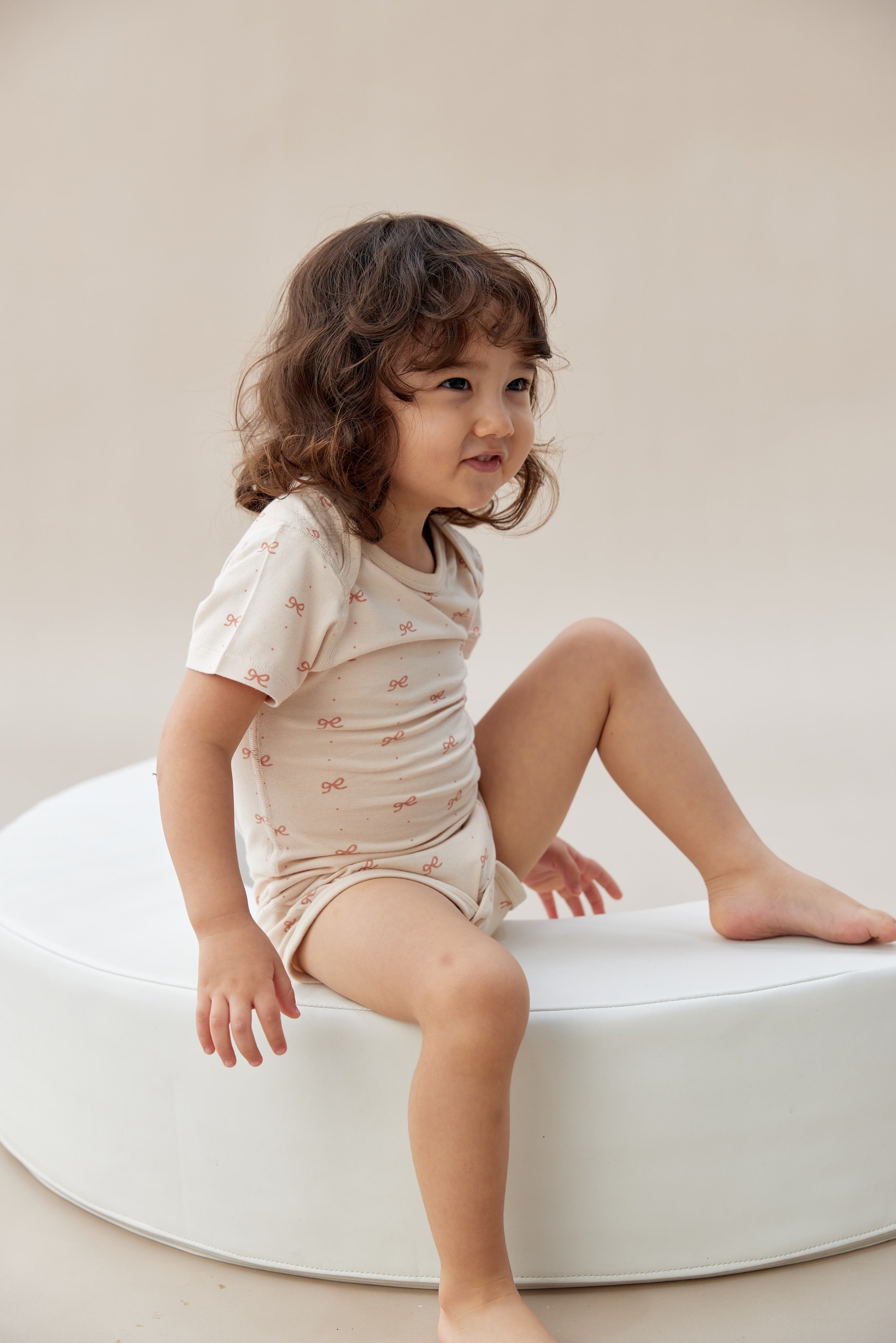 Child sitting on a white cushion against a plain background