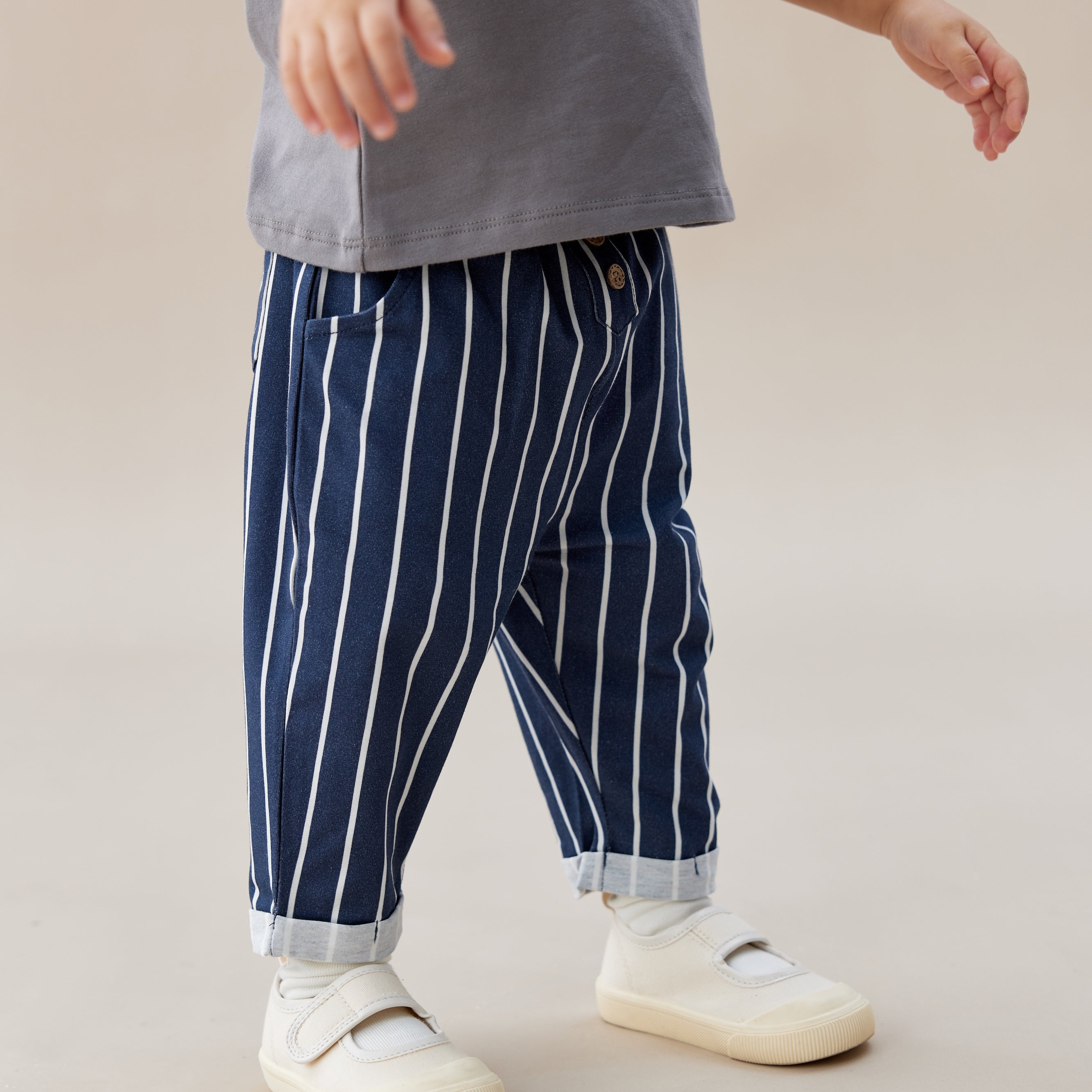 Child wearing a gray shirt with a colorful design and blue striped pants on a beige background