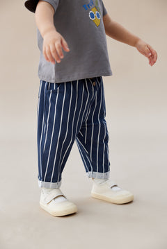 Child wearing a gray shirt with a colorful design and blue striped pants on a beige background