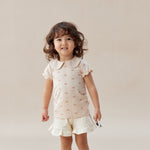 Young girl wearing a light pink dress with ruffled shorts on a plain background