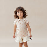 Young girl wearing a light pink dress with ruffled shorts on a plain background