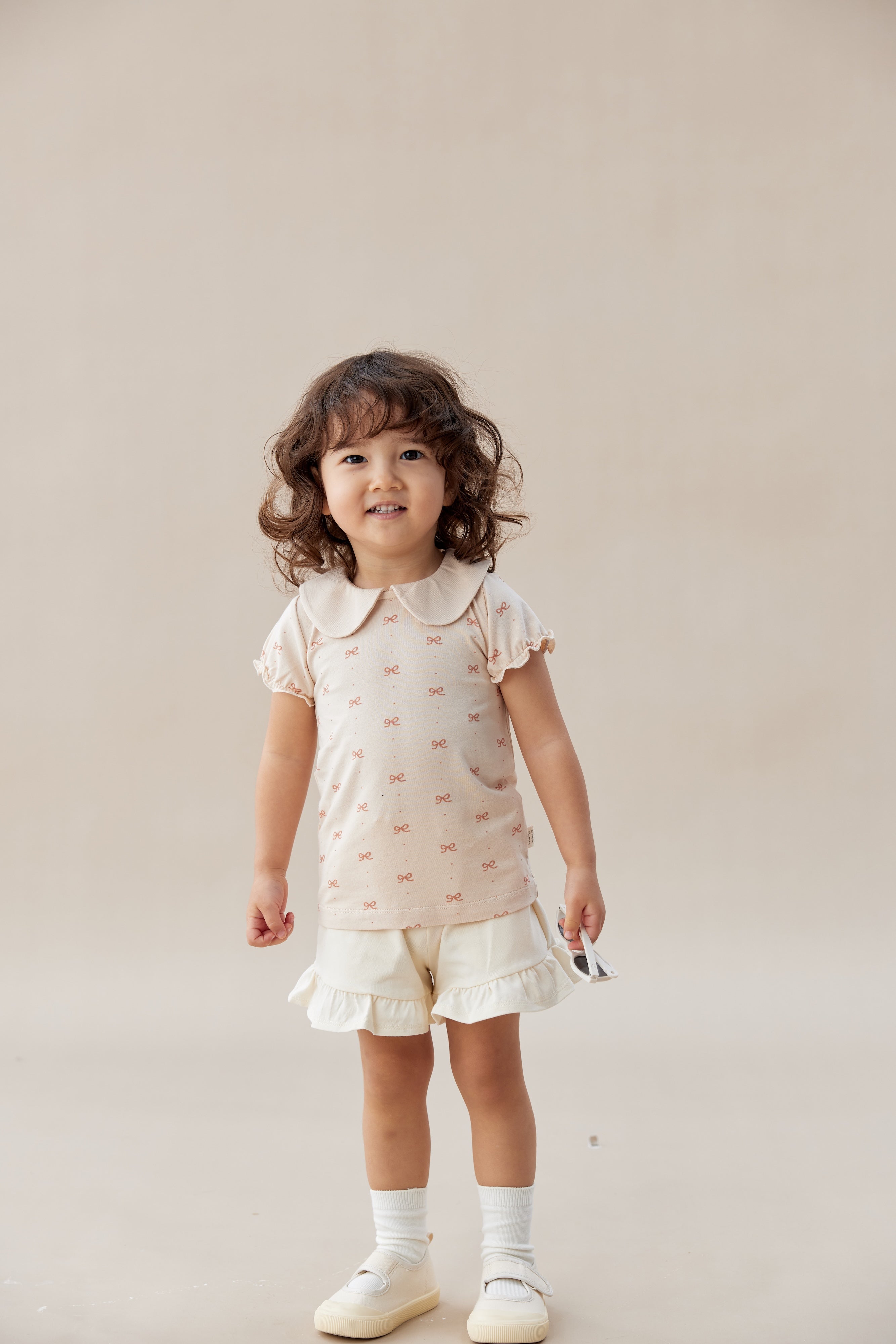 Young girl wearing a light pink dress with ruffled shorts on a plain background