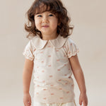 Child wearing a white outfit with ruffled details against a plain background