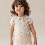 Child wearing a white outfit with ruffled details against a plain background