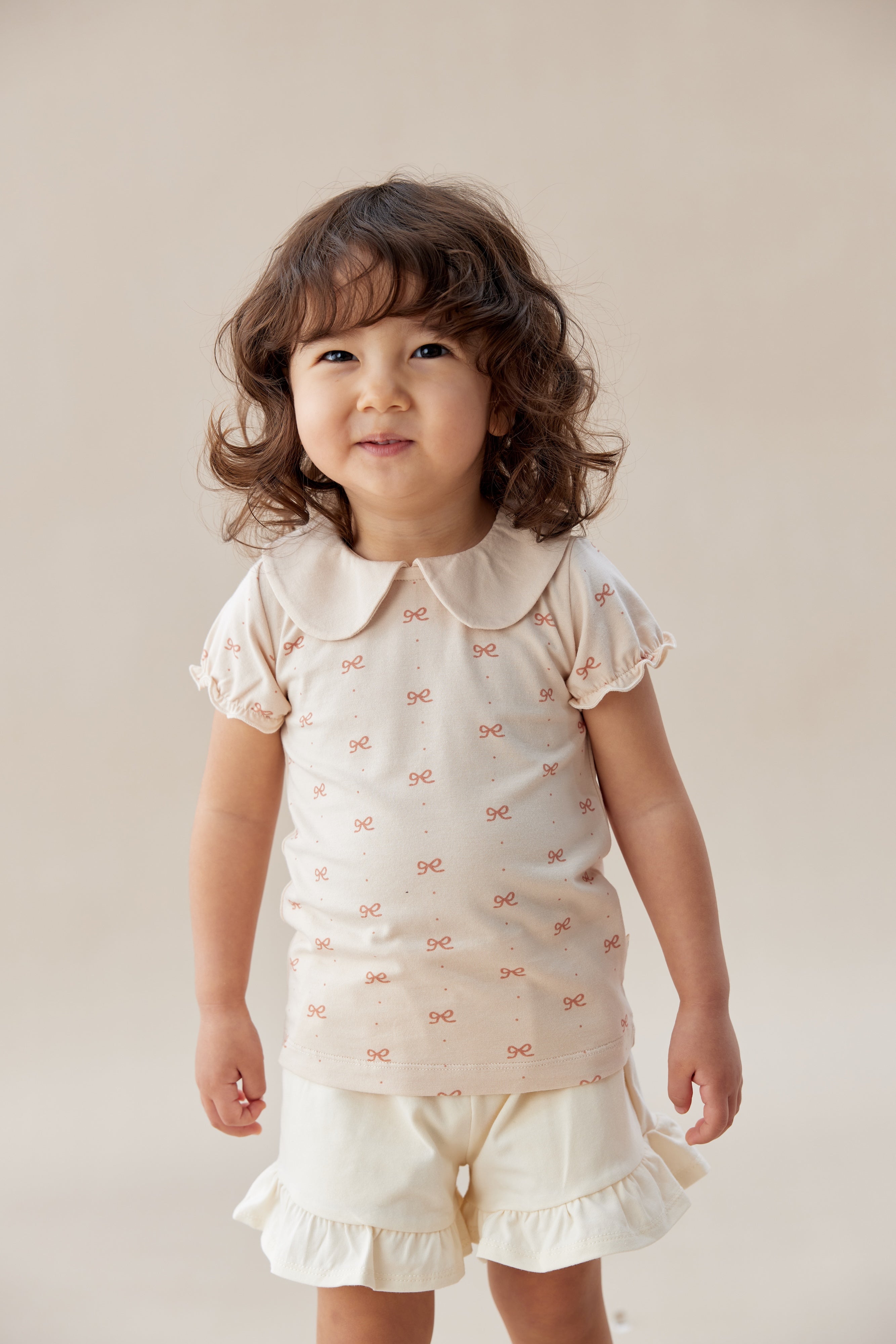 Child wearing a white outfit with ruffled details against a plain background