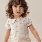 Child wearing a white blouse with a pattern on a plain background