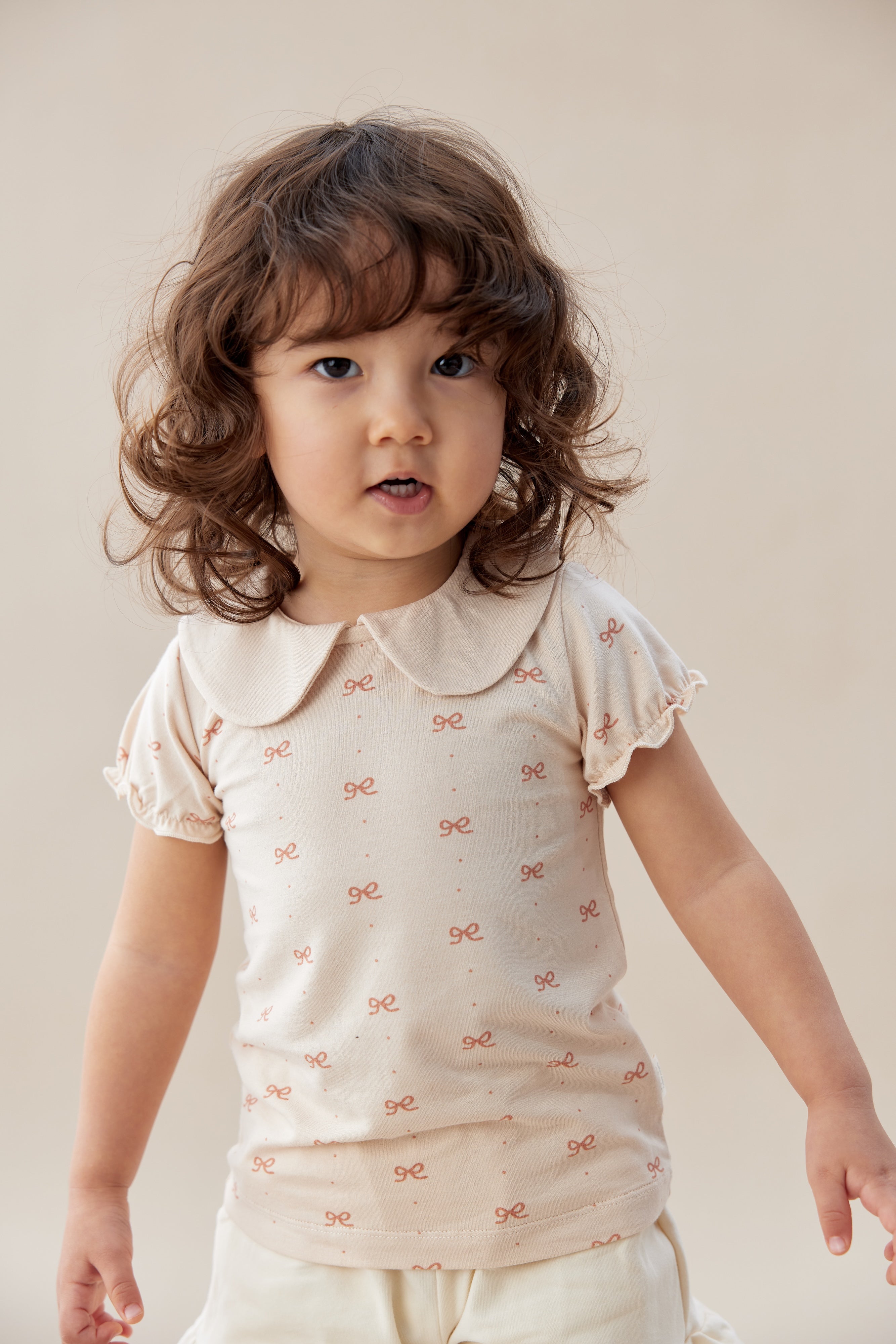 Child wearing a white blouse with a pattern on a plain background