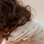 Person wearing a white nightgown with red patterns, sitting on a bed.