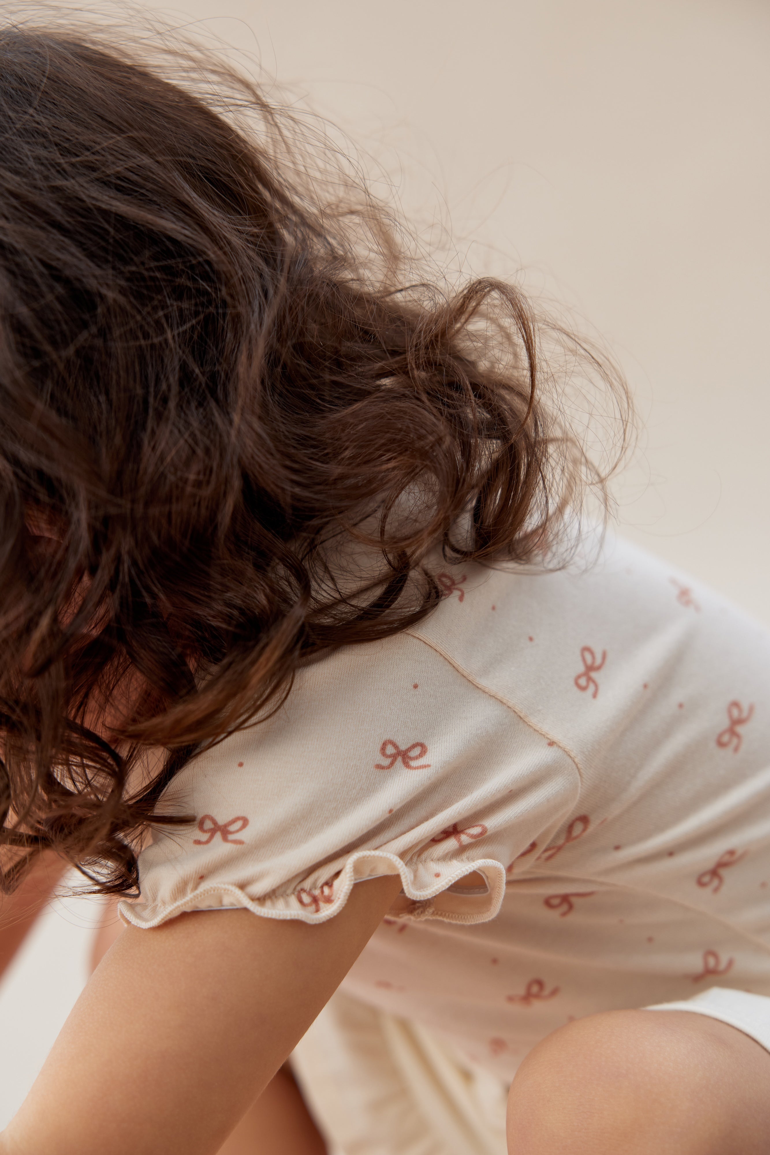 Person wearing a white nightgown with red patterns, sitting on a bed.
