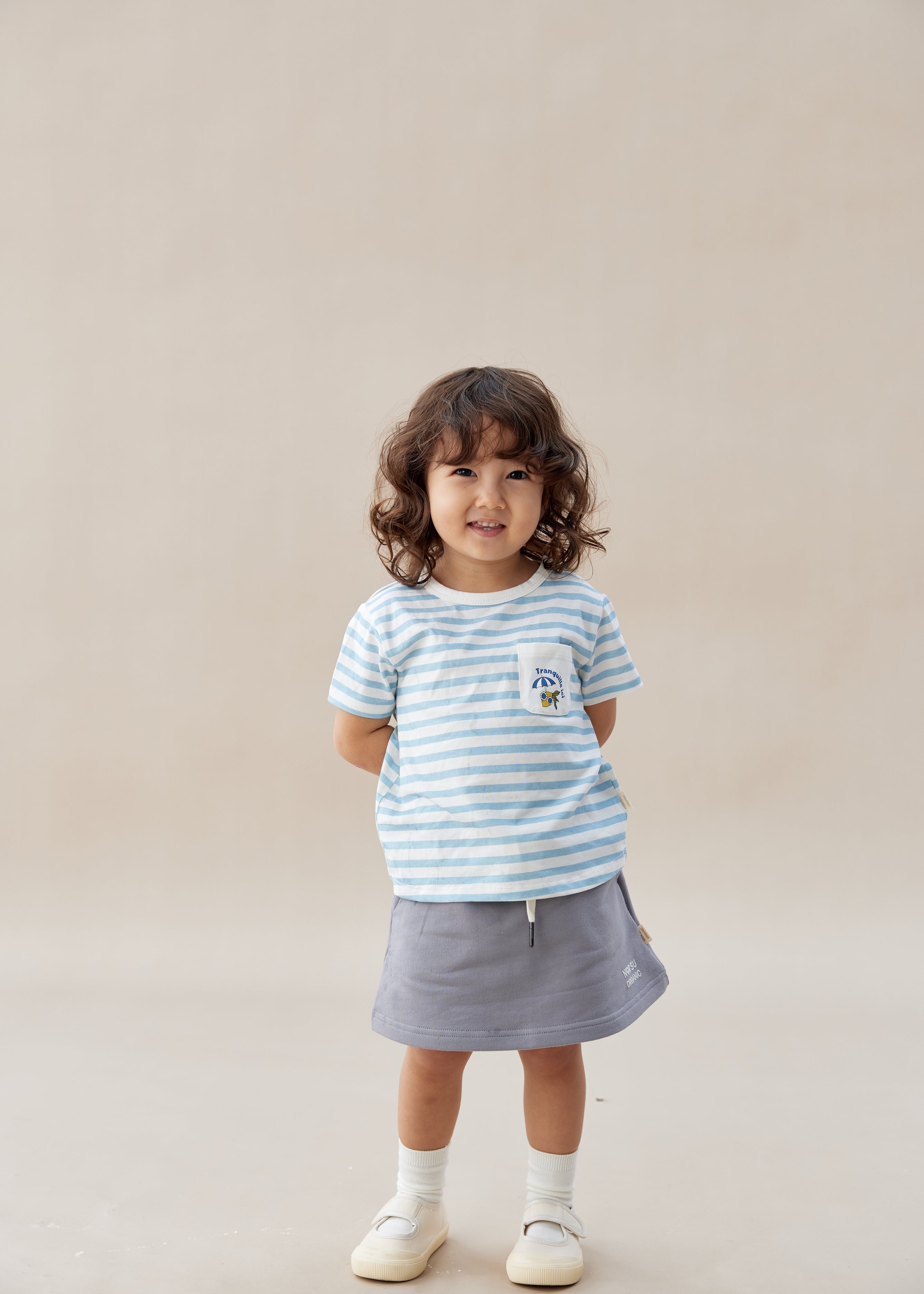 Child wearing a striped shirt and skirt on a plain background