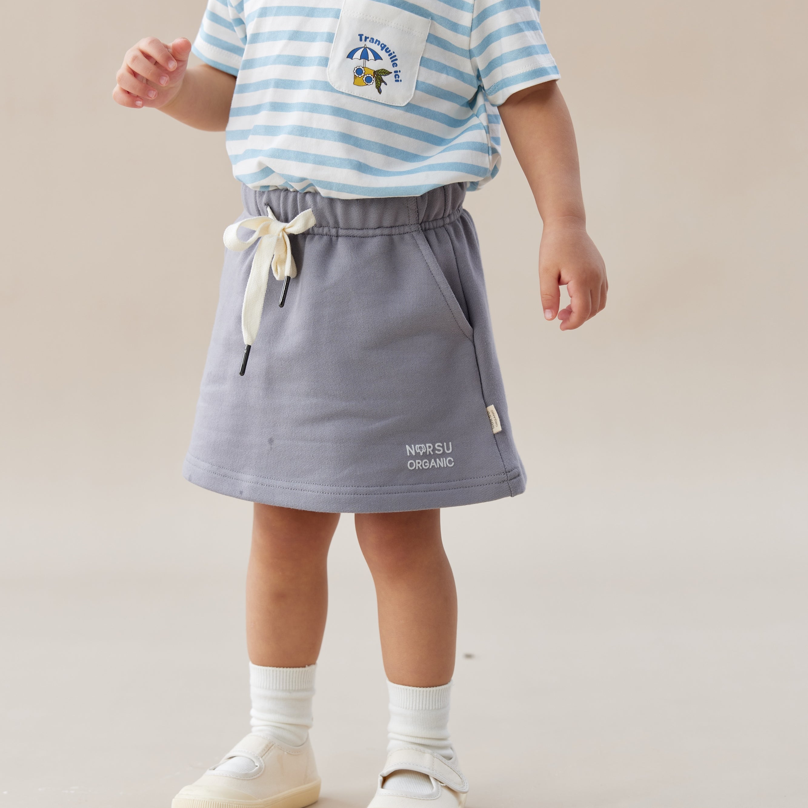 Child wearing a striped shirt and gray skirt on a plain background