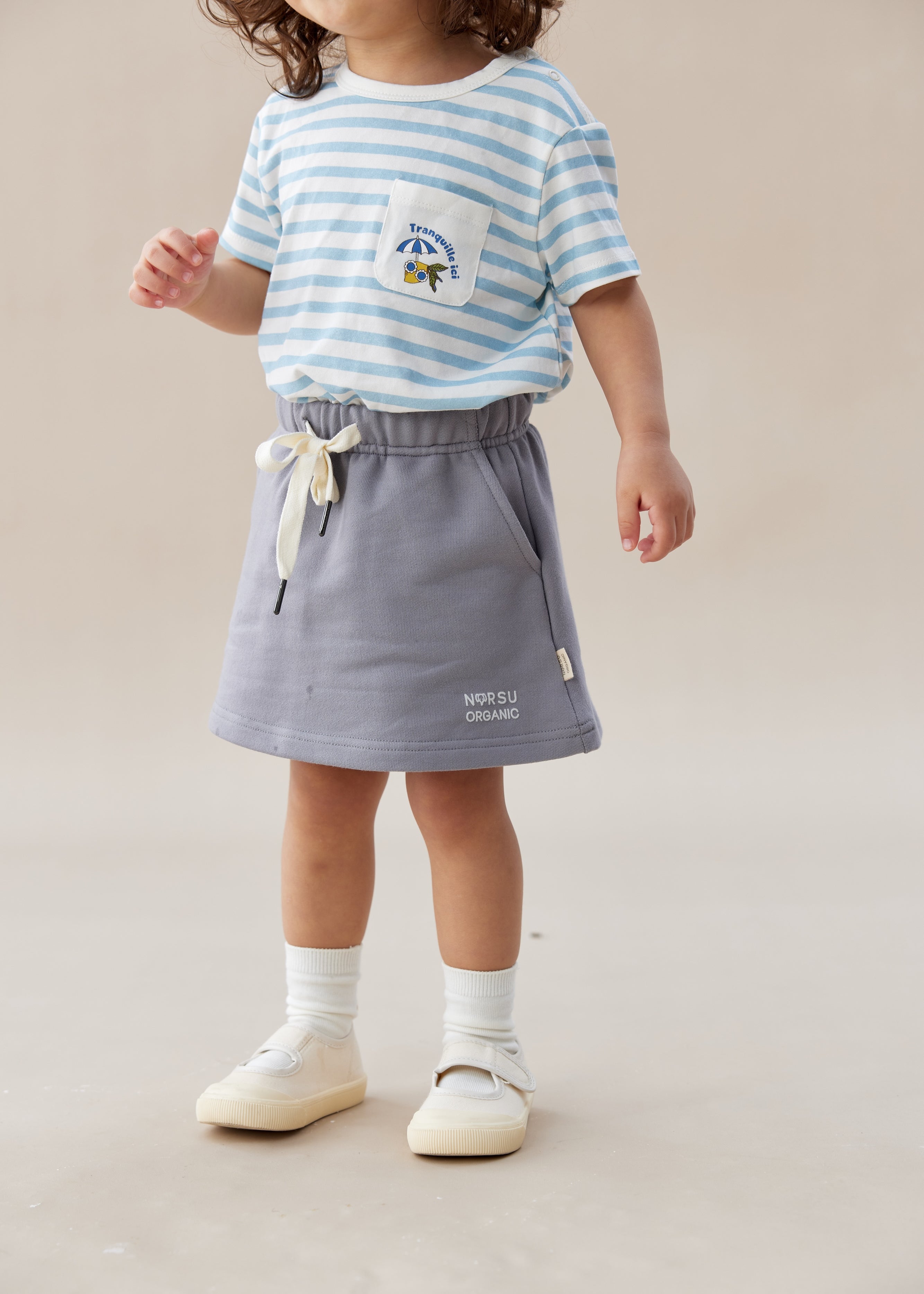 Child wearing a striped shirt and gray skirt on a plain background