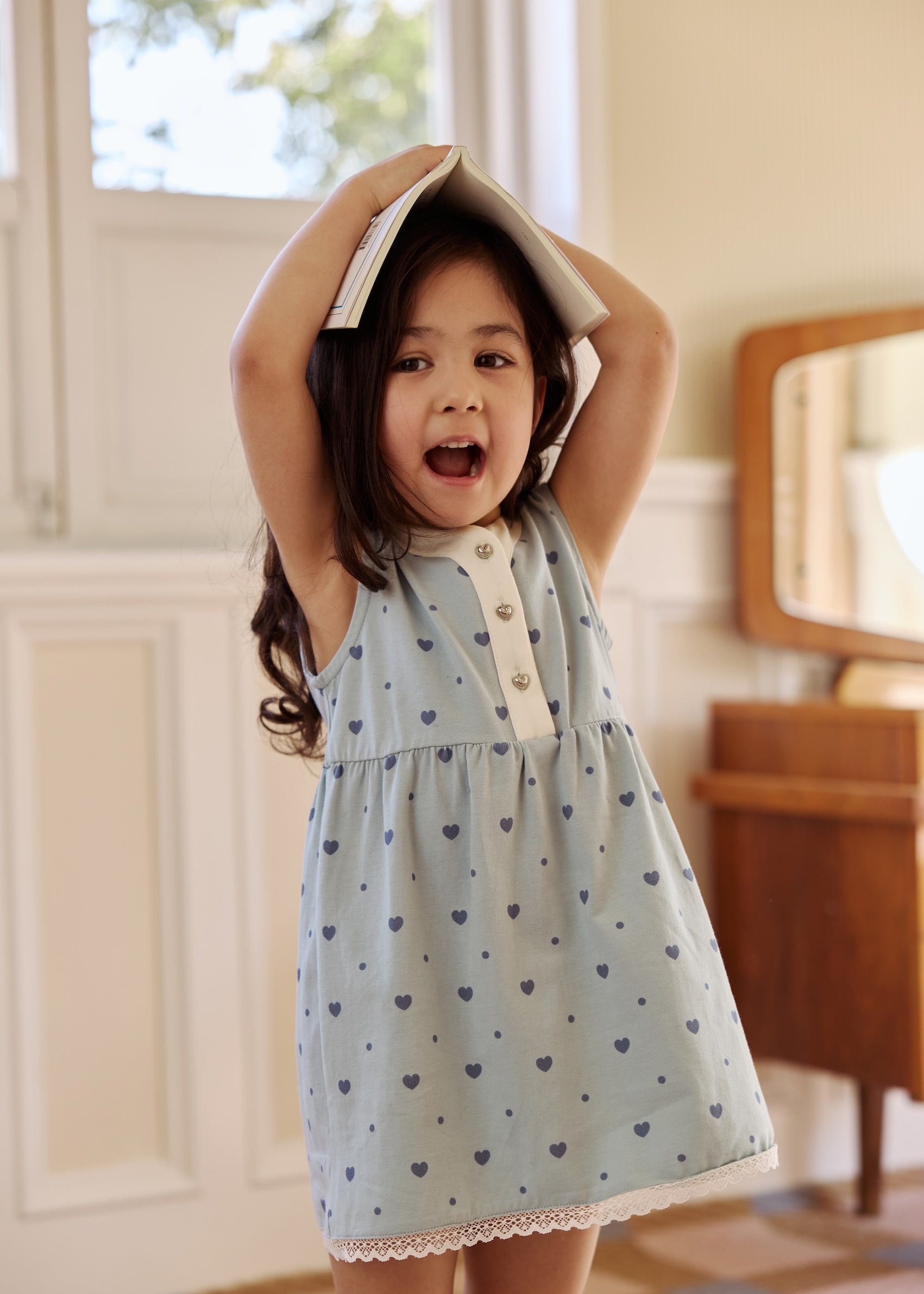  A little girl in a blue heart-patterned dress proudly holds her head up high, radiating joy and confidence.
