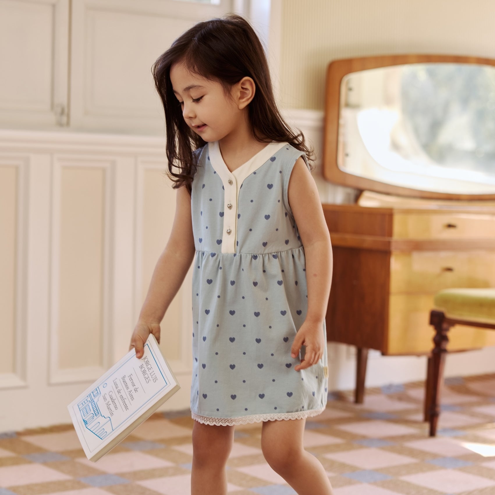  A little girl in a blue heart-patterned dress happily holds a book, ready for a story adventure