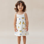Child wearing a white dress with colorful patterns on a beige background