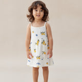 Child wearing a white dress with colorful patterns on a beige background