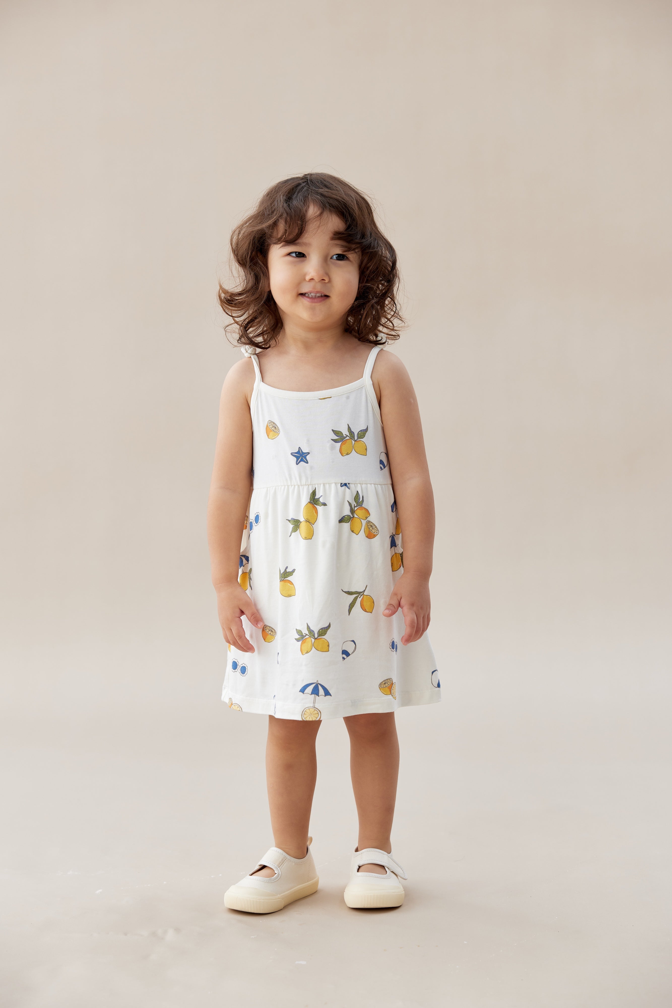 Child wearing a white dress with colorful patterns on a beige background