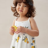 Child wearing a white dress with lemon prints, holding a lemon against a plain background