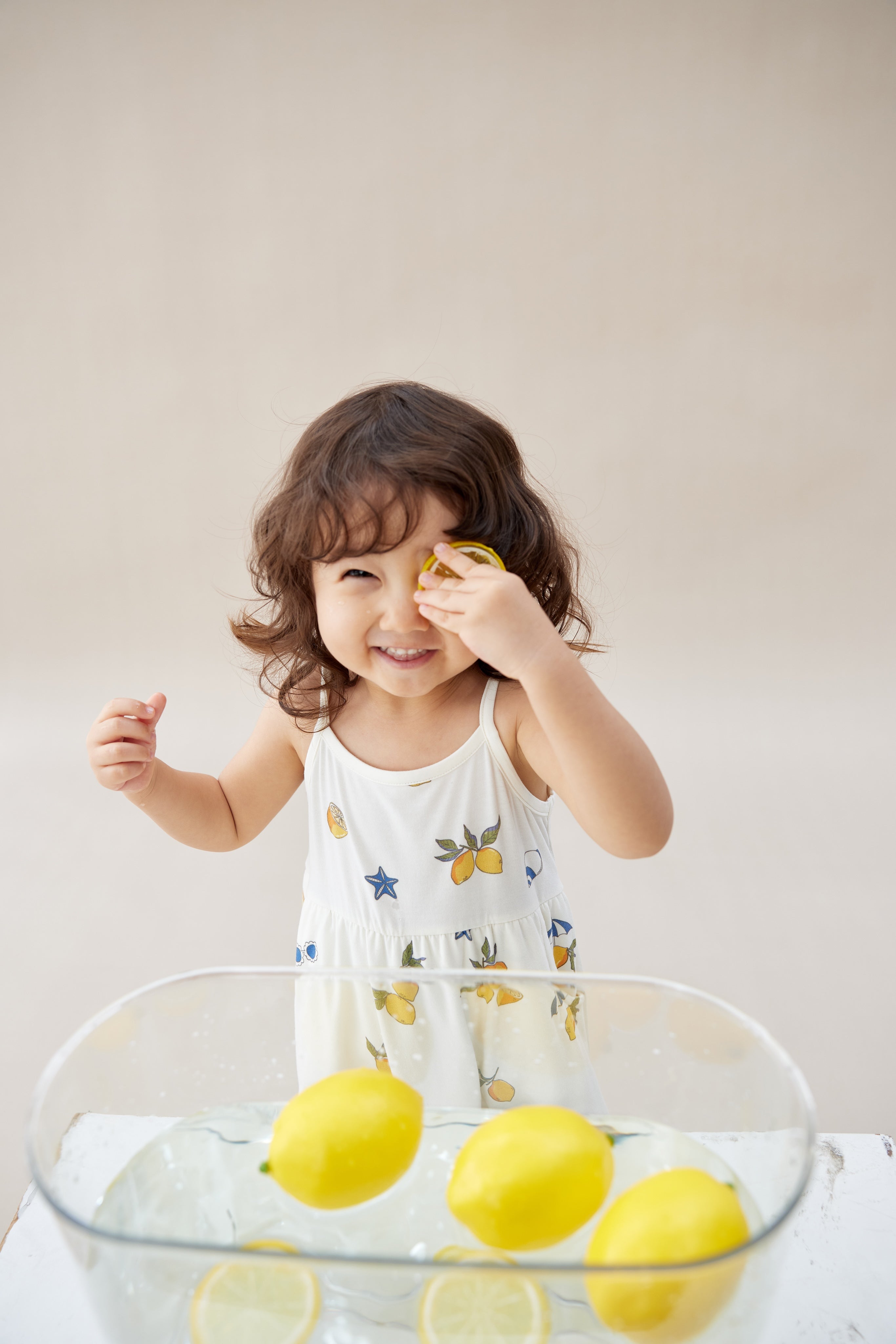 Child playing with lemons in a glass bowl on a light background