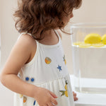 Child wearing a white dress with fruit patterns in a kitchen setting