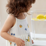 Child wearing a white dress with fruit patterns in a kitchen setting