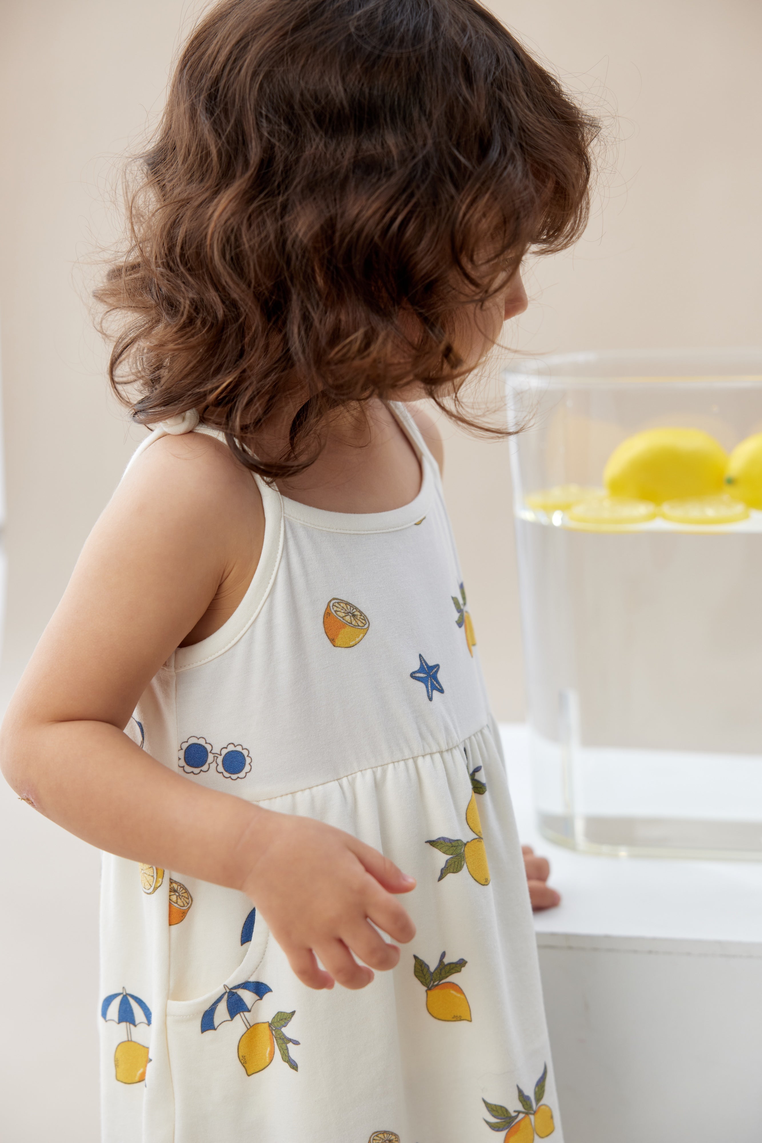 Child wearing a white dress with fruit patterns in a kitchen setting