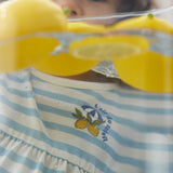 Child holding lemons with a striped dress featuring lemon design