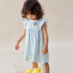 Young girl in a blue and white striped dress standing next to a glass table with lemons on a plain background