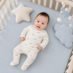 Baby lying on a crib with blue bedding, star pillow, and cloud-shaped pillow.