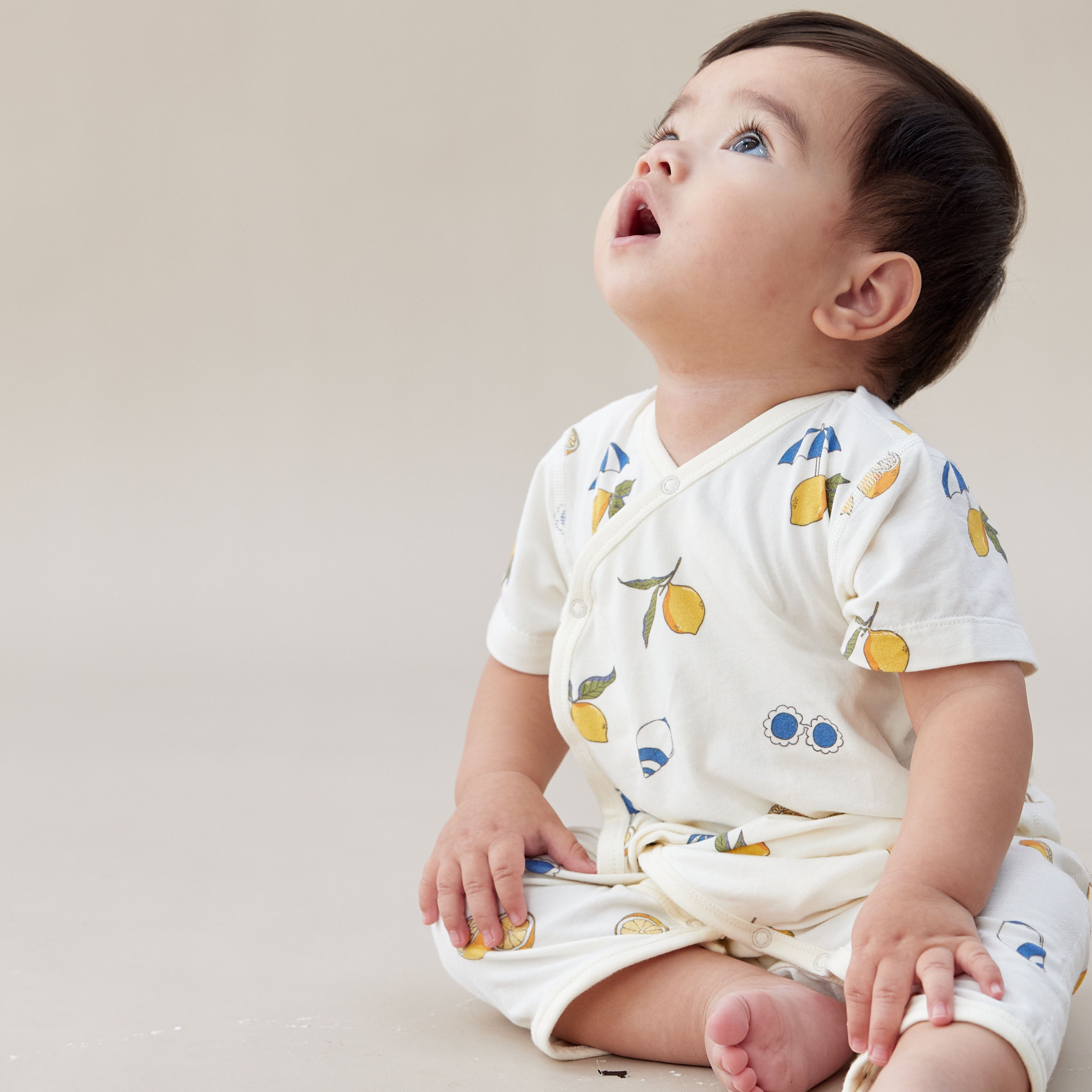 Baby wearing a white outfit with colorful patterns on a plain background