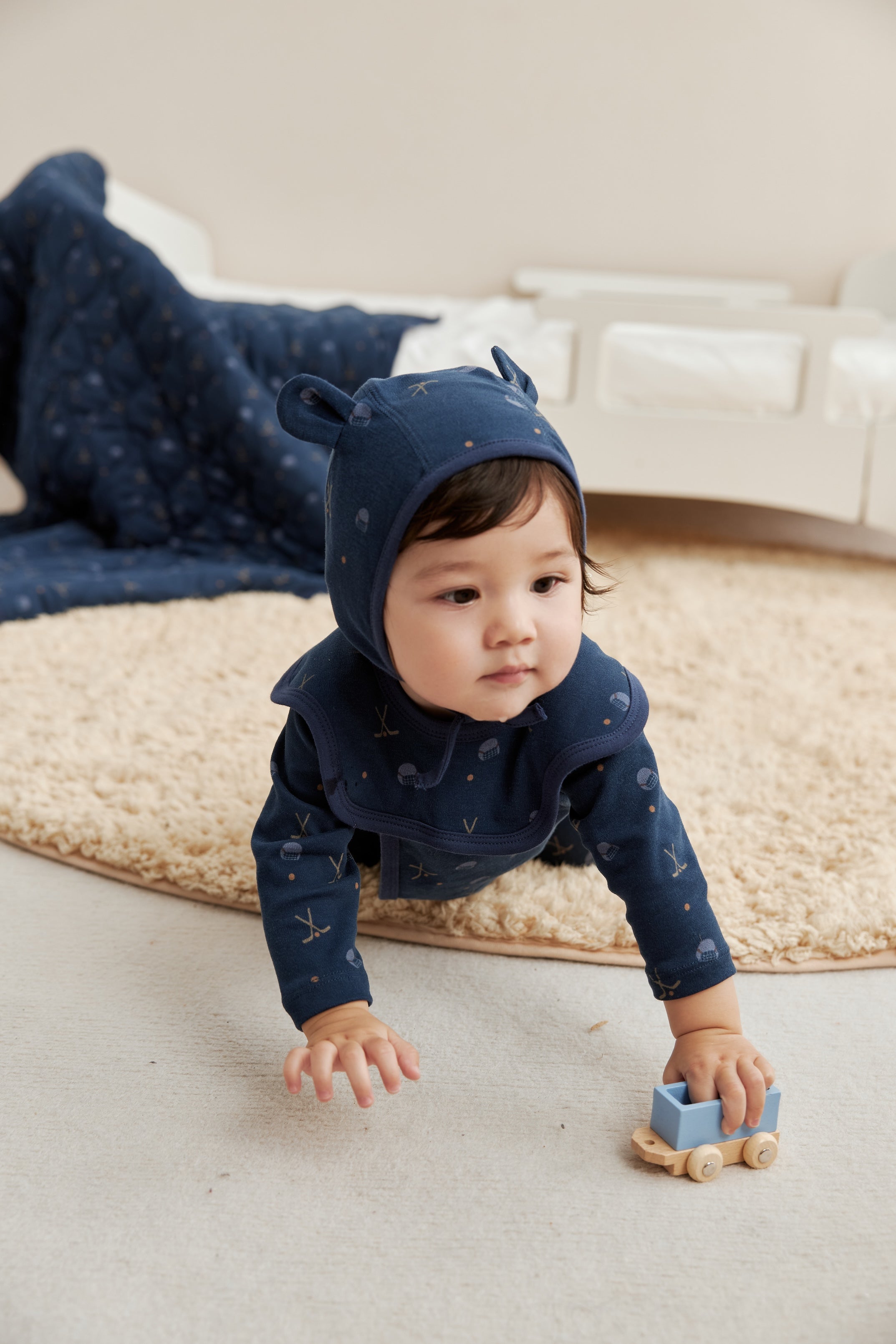 Baby in a navy blue outfit with bear ears playing on a rug.