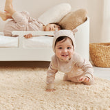 Two children in matching outfits playing on a beige rug.