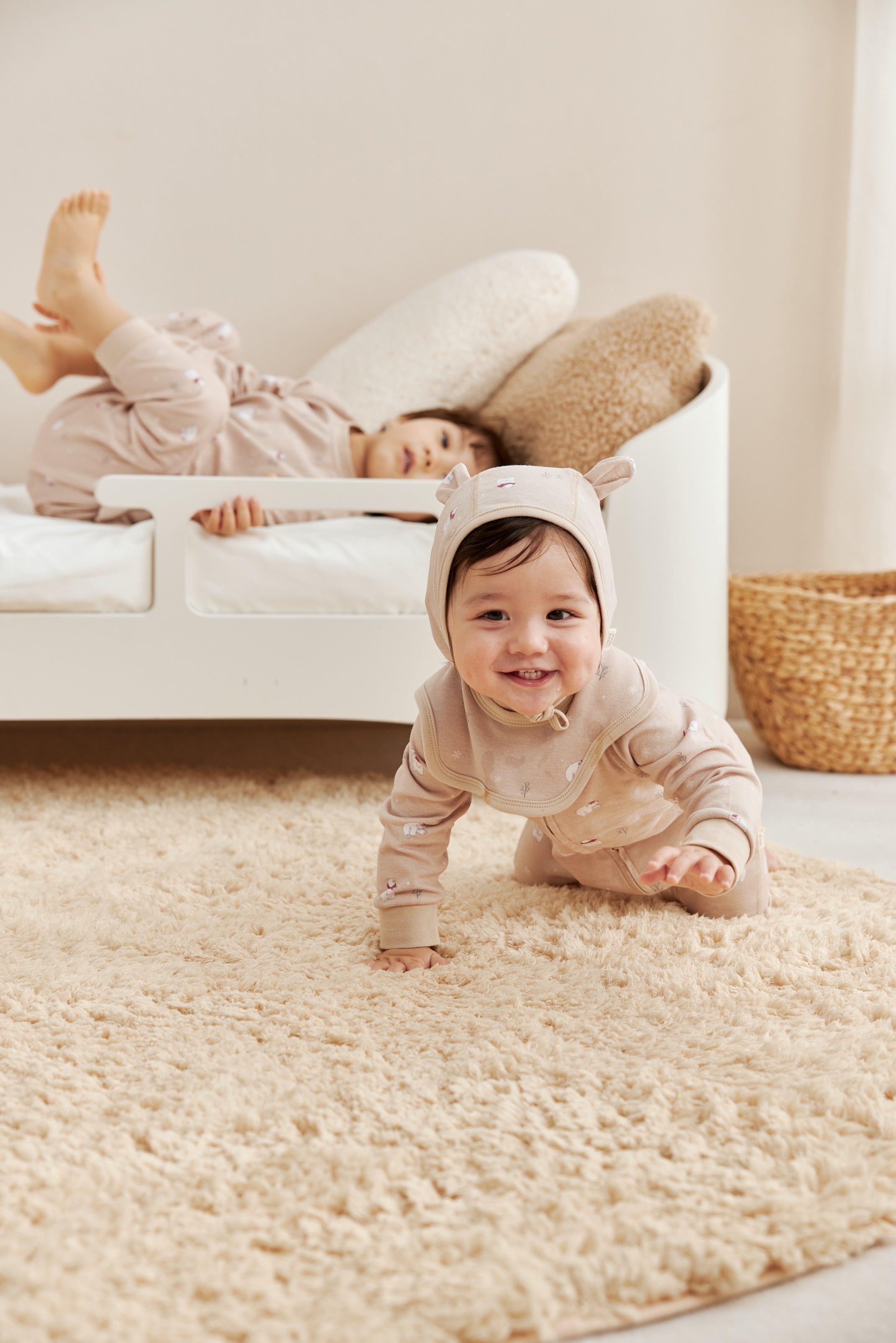 Two children in matching outfits playing on a beige rug.