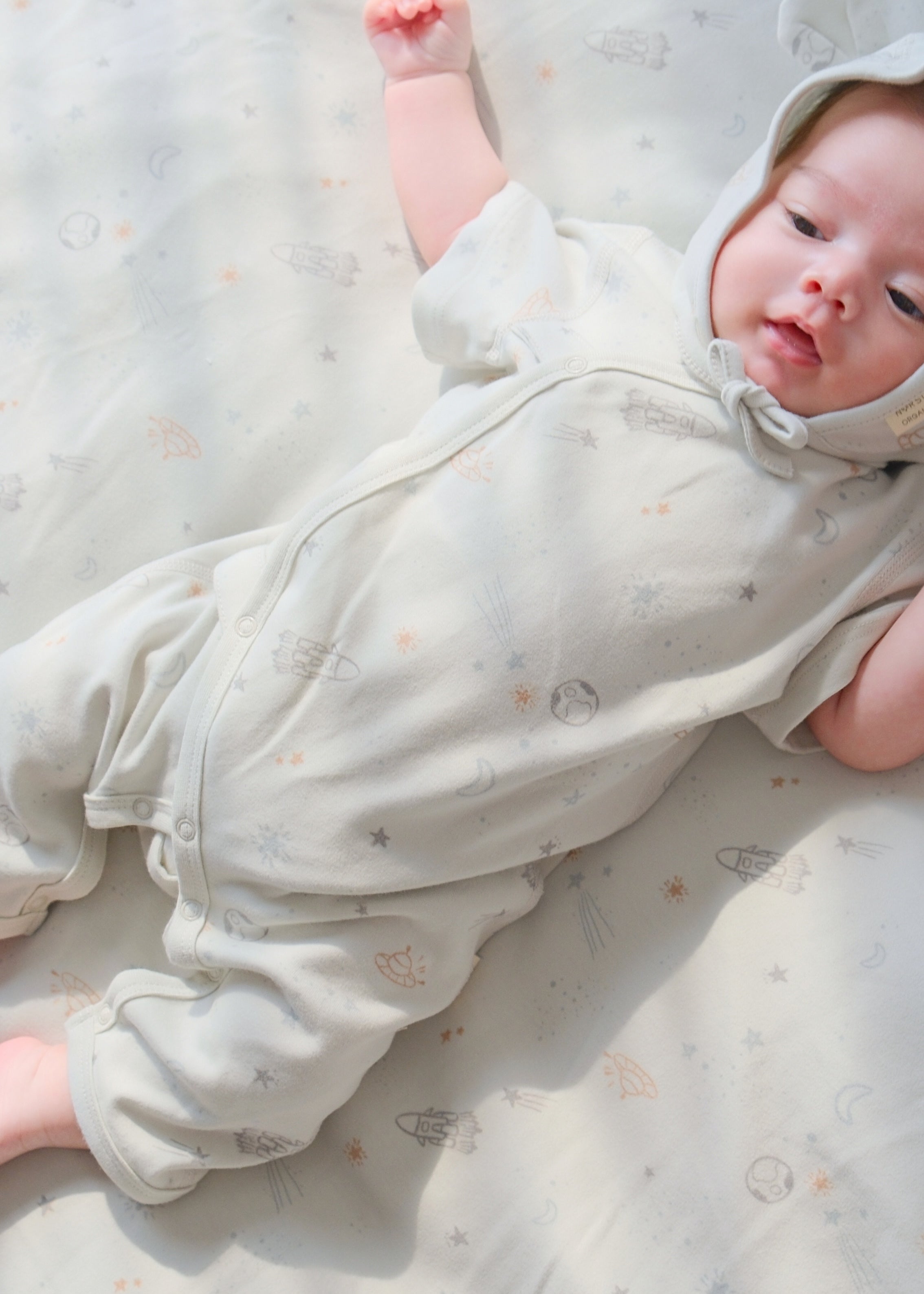 a baby lying on the bed and wear space bonnet hat and organic space kimono sleeper