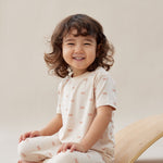 Child sitting on a beige surface wearing a white outfit with small patterns.