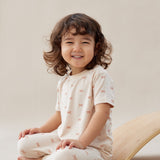 Child sitting on a beige surface wearing a white outfit with small patterns.