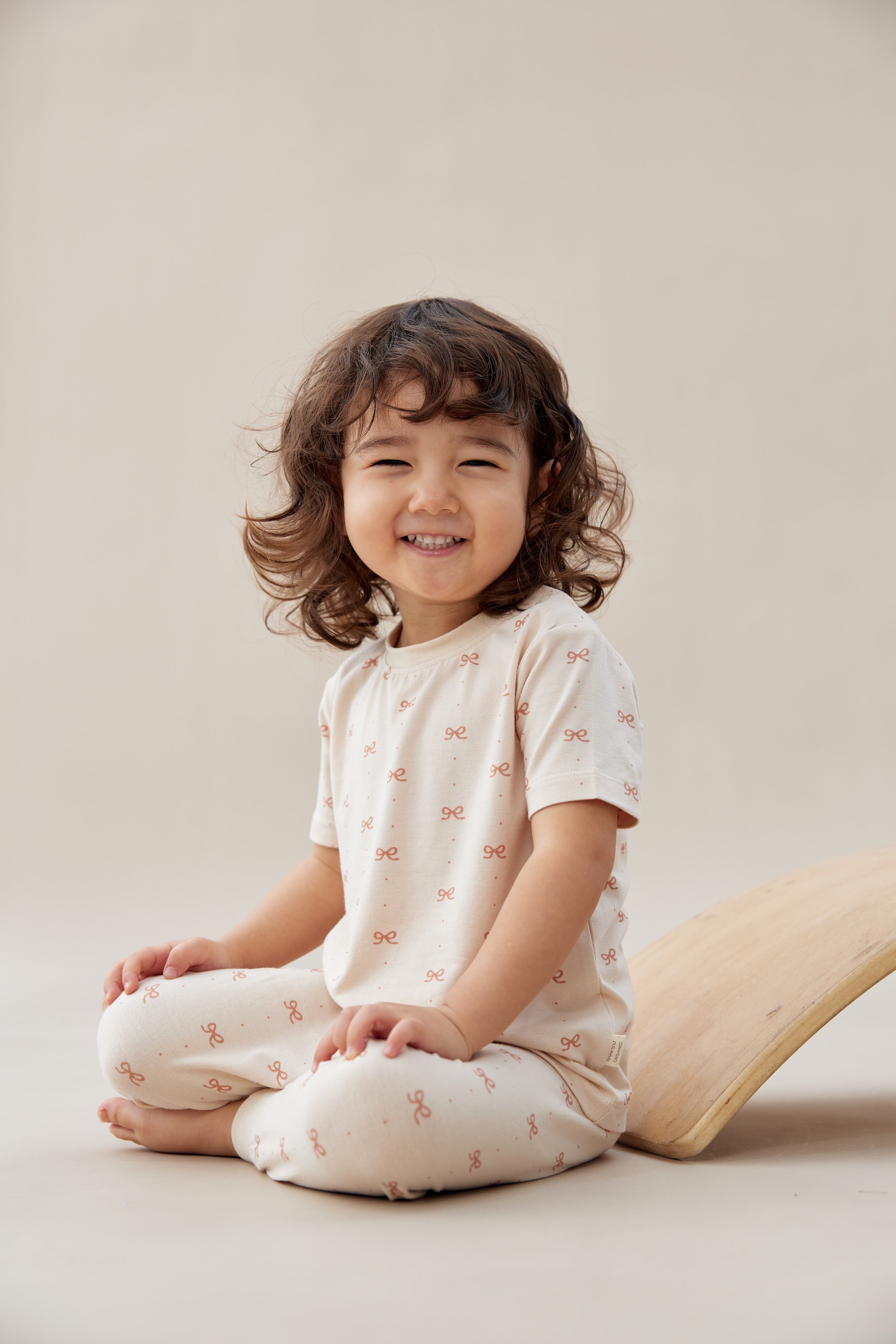 Child sitting on a beige surface wearing a white outfit with small patterns.