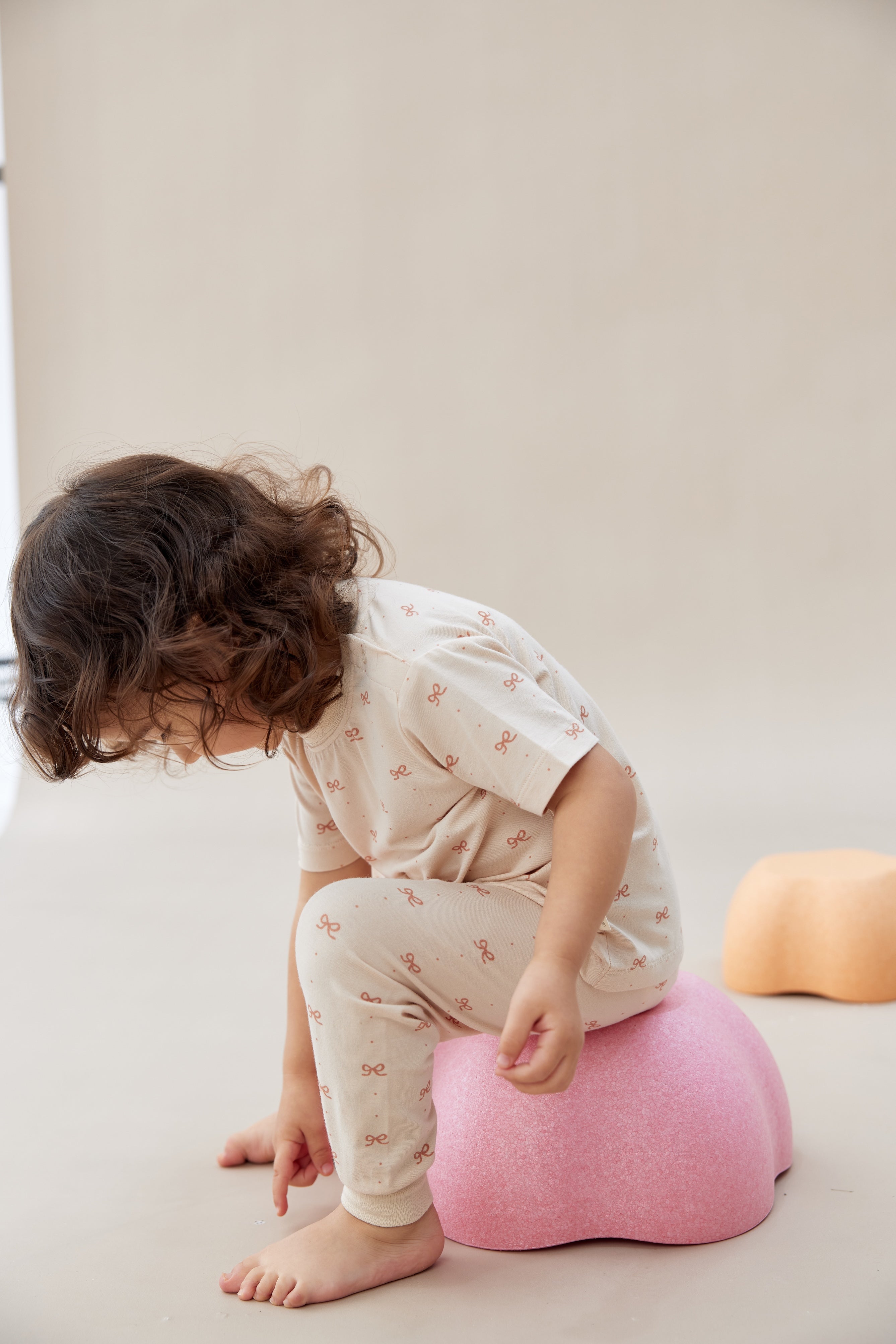Child sitting on a pink cushion on a plain background