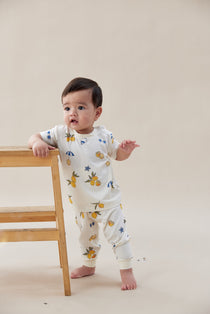 Baby standing on a light-colored floor wearing a white onesie with colorful patterns.