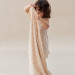 Child holding a beige blanket with small patterns on a plain background