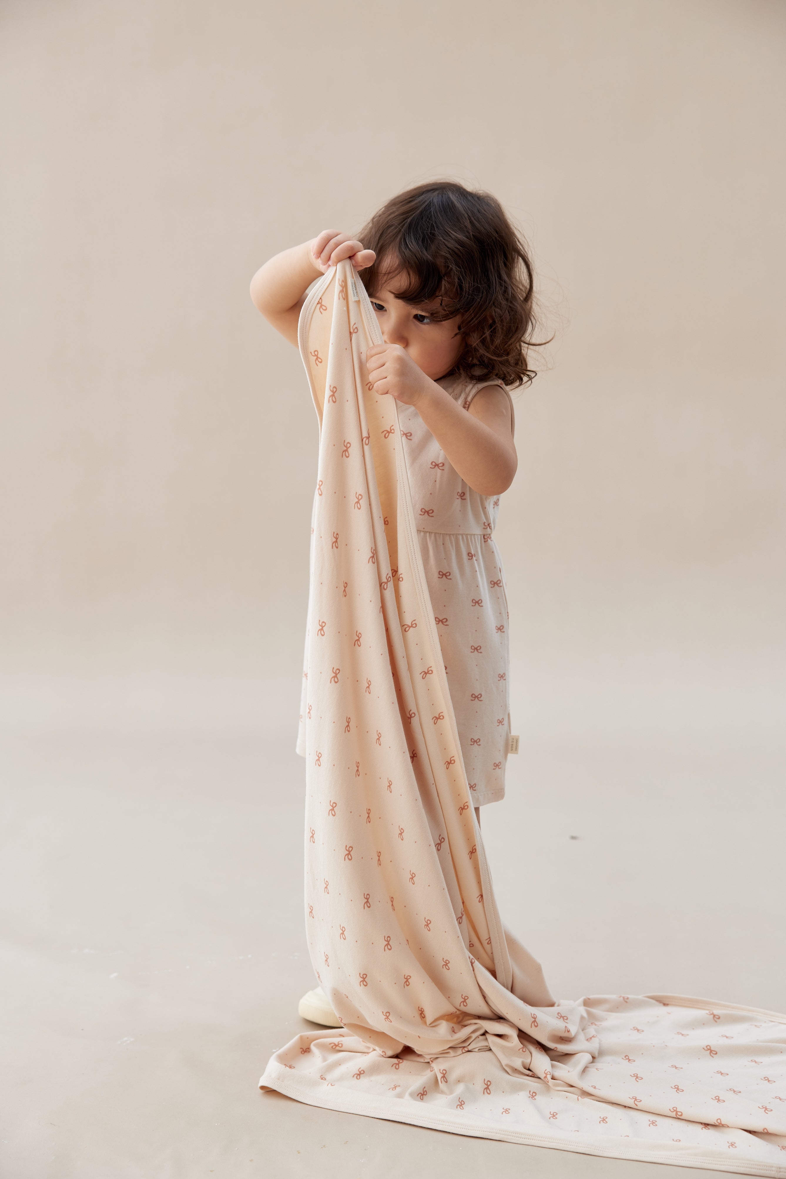 Child holding a beige blanket with small patterns on a plain background