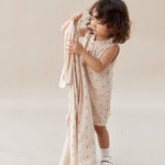 Child holding a pink swaddle with subtle pattern on a plain background