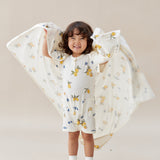 Child wearing a floral dress with a matching blanket, standing against a plain background