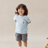 Child wearing a striped shirt and shorts standing against a plain background