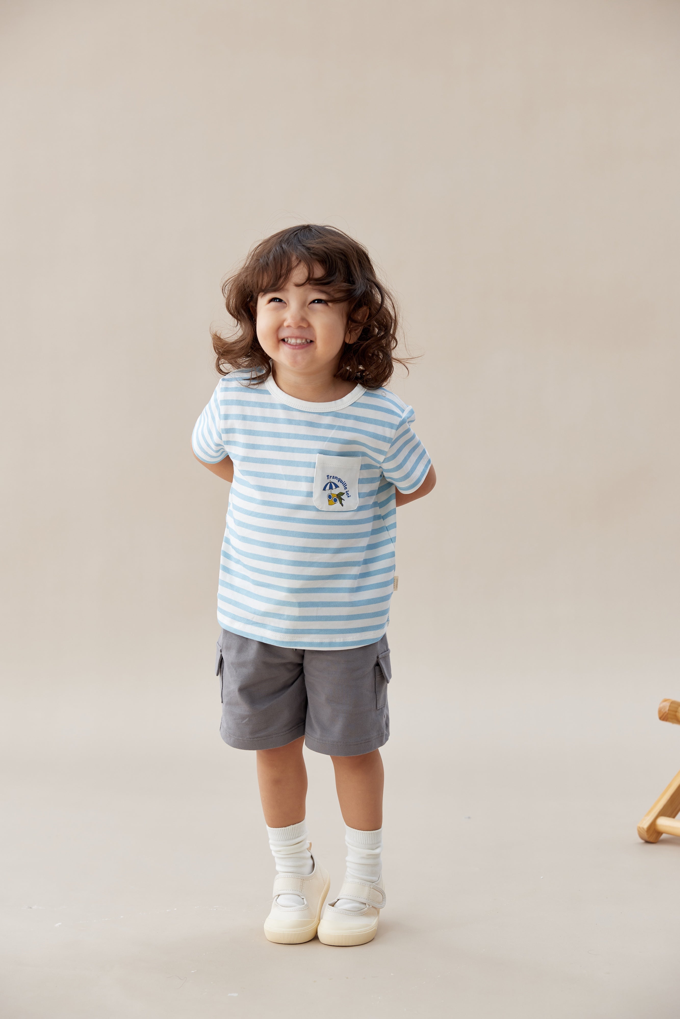 Child wearing a striped shirt and shorts standing against a plain background