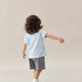Child wearing a striped shirt and shorts standing against a plain background