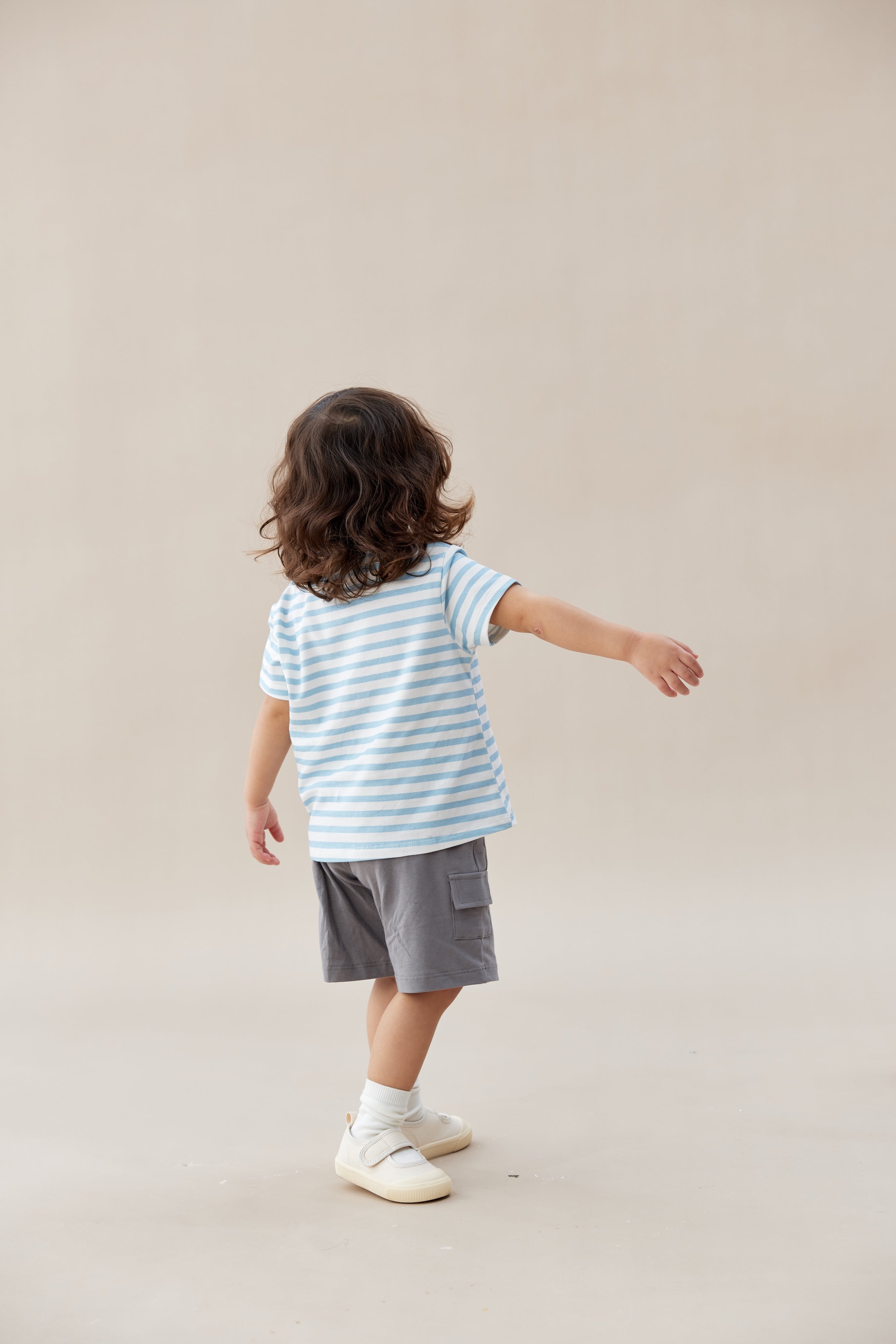 Child wearing a striped shirt and shorts standing against a plain background