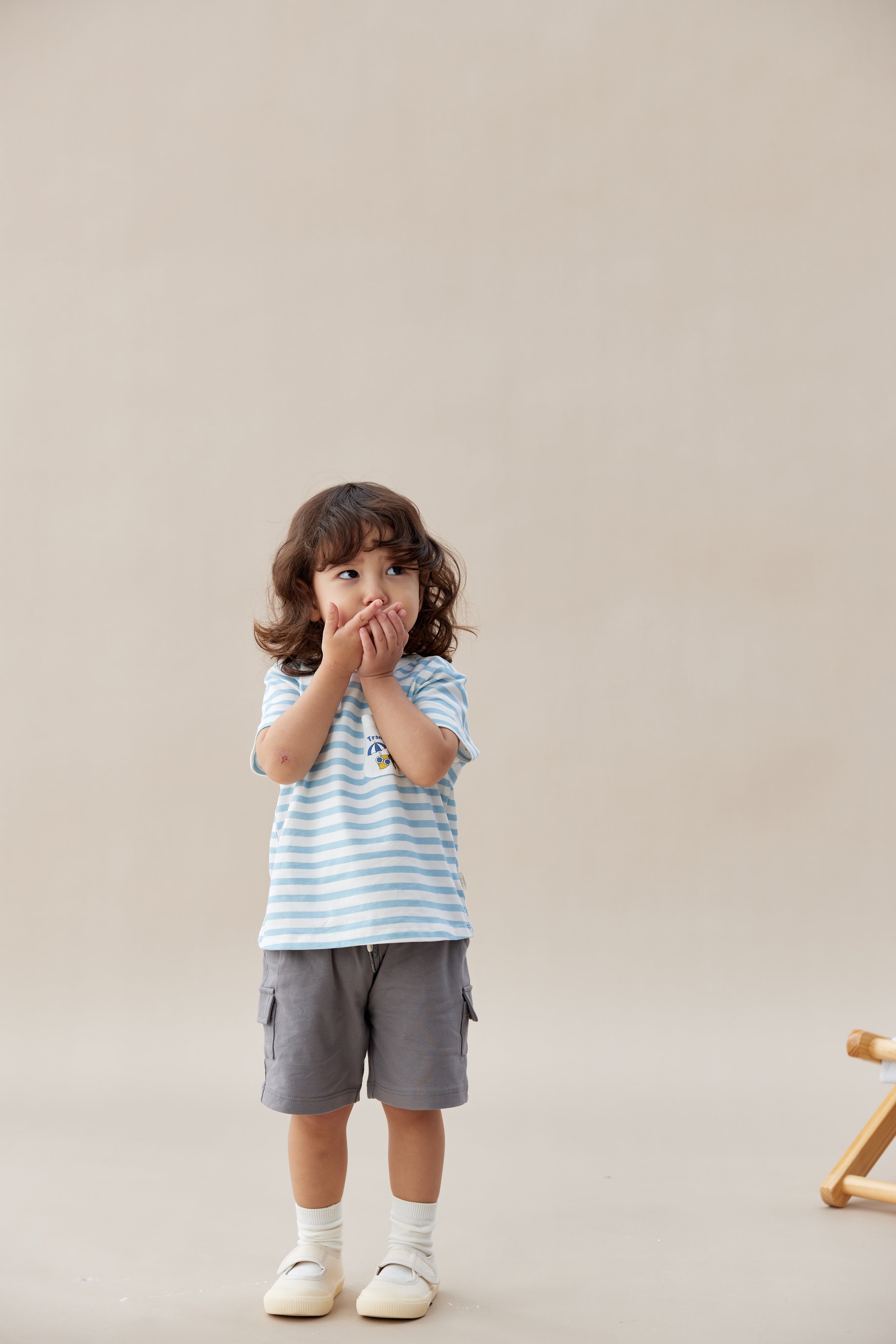 Child wearing a striped shirt and gray shorts on a plain background
