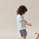 Child wearing a striped shirt and shorts standing on a beige background